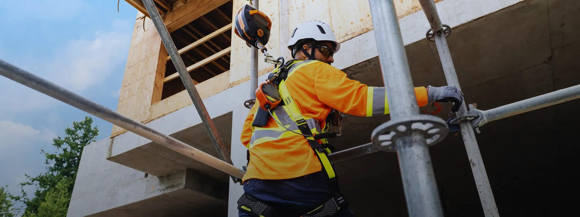 Worker climbing scaffolding wearing a SureWerx fall protection harness on a construction site