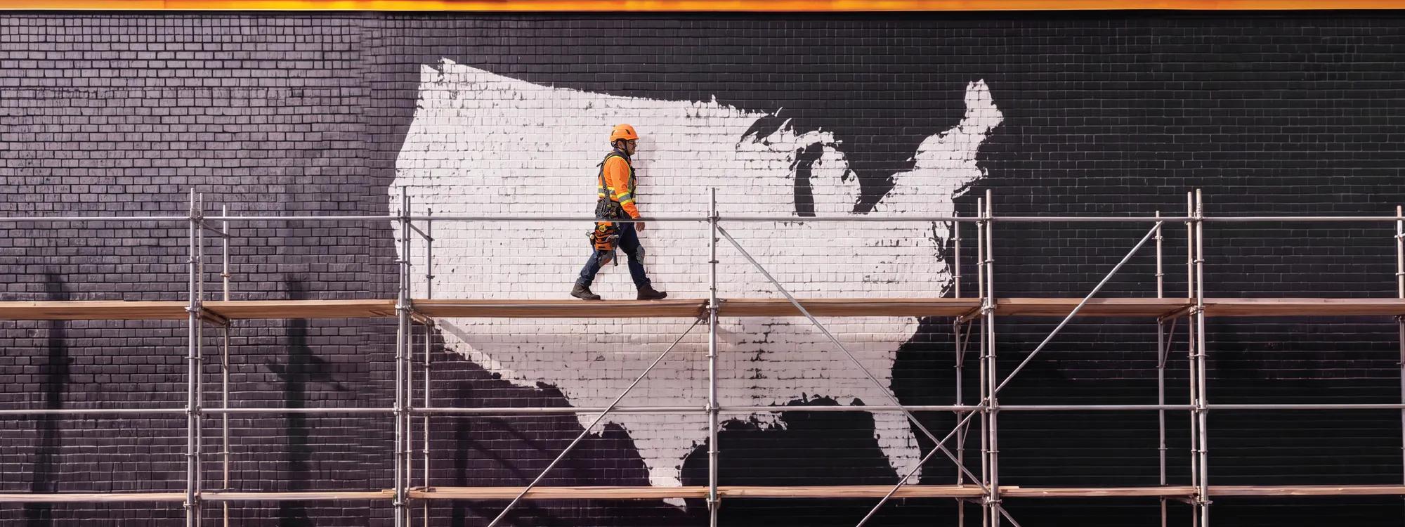 Construction worker walking across scaffolding in front of a mural of the United States